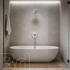 Minimalist bathroom with a white freestanding tub, wall-mounted shower, gray tiled walls, towel on the left, and a pebble floor with a wooden mat.