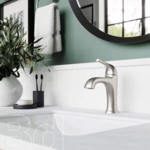 Modern bathroom sink area featuring a brushed metal faucet, white countertop, green wall, round mirror, plant, and towels.