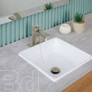 Modern bathroom sink setup with a brushed metal faucet, gray countertop, and decorative plants in beige pots in the background.