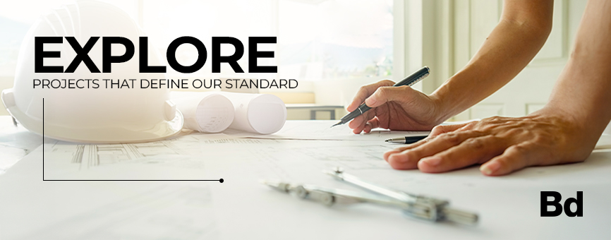 Banner: hands sketching on blueprints at a construction desk with a hard hat and tools; overlaid text reads 'EXPLORE PROJECTS THAT DEFINE OUR STANDARD' with the Bd logo in the corner.