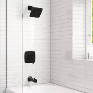 Black square rainfall shower head and matching dark faucet fixtures mounted on white-tiled shower wall beside a tub.