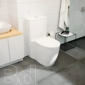 Contemporary bathroom with a white one-piece toilet, a wooden vanity with a white vessel sink, and a black metal side table holding a green bottle and a notebook beside a towel hanging on the wall.